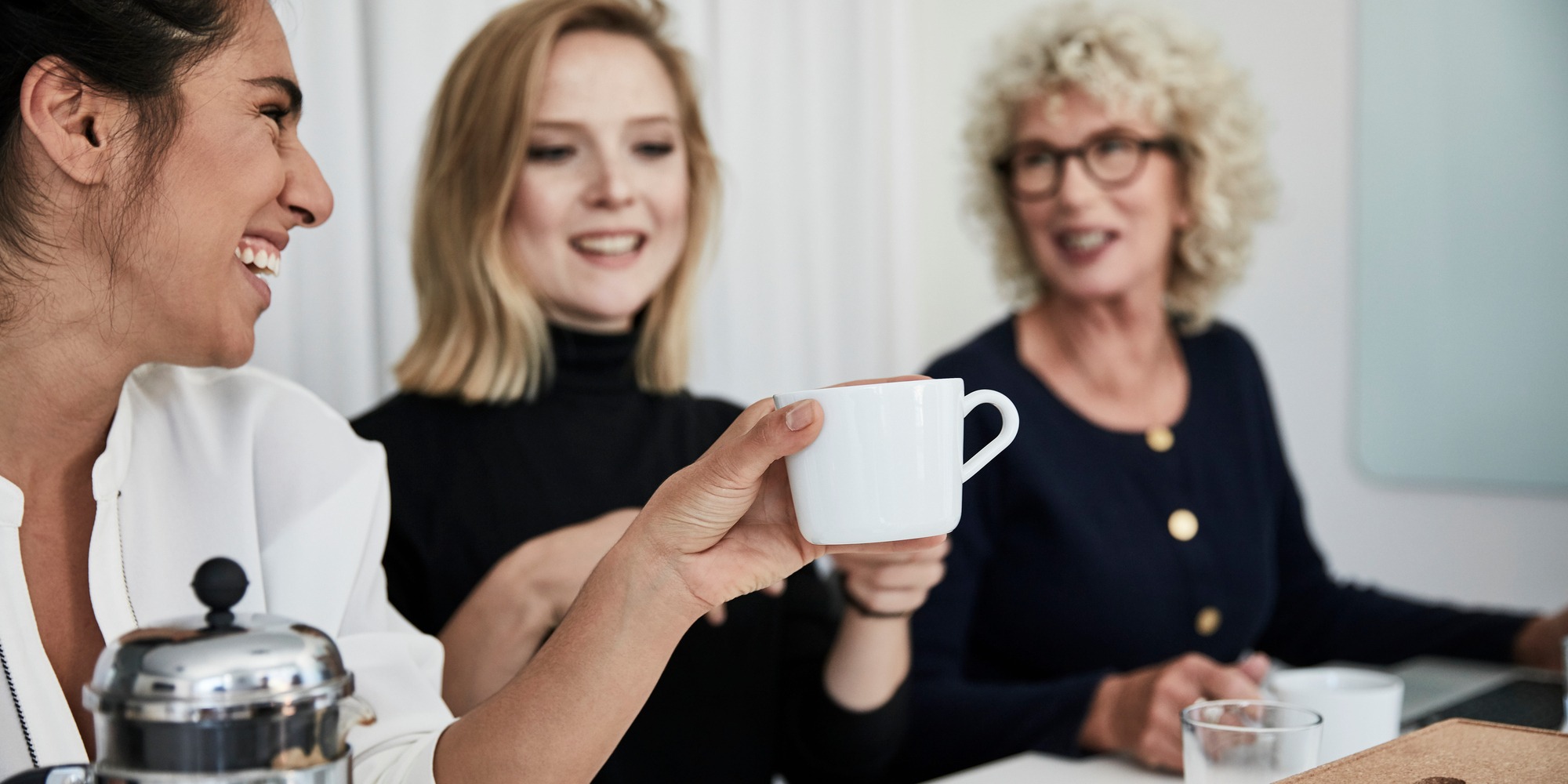 Tre kvinnor i ett mötesrum häller upp kaffe