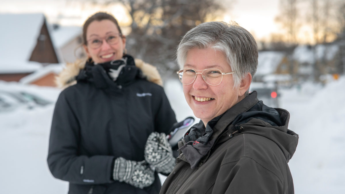 Två leende kvinnor står utomhus i snölandskap.