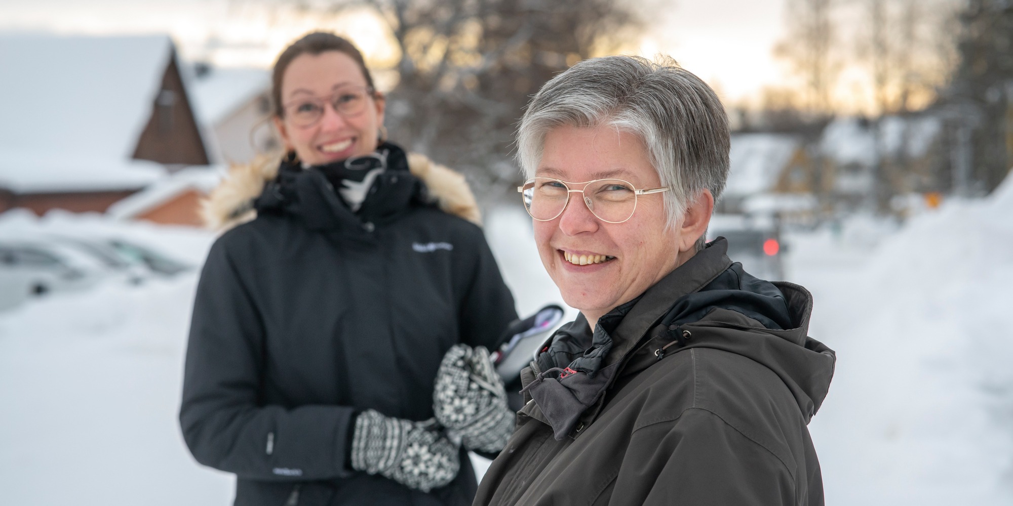 Två leende kvinnor står utomhus i snölandskap.