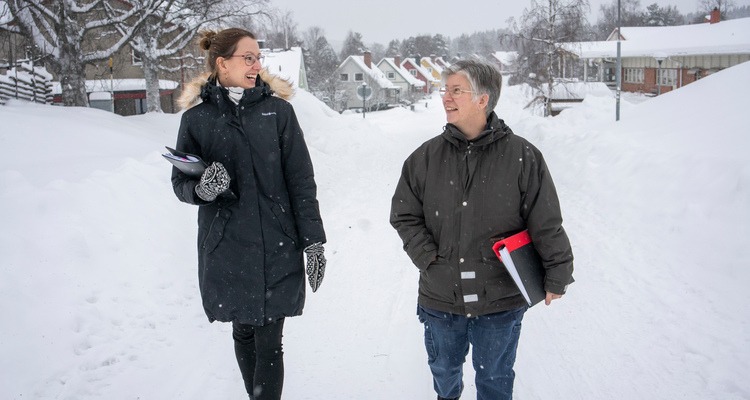 Två kvinnor går bredvid varandra i ett snöigt villaområde.