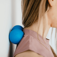 En bild på en person som håller på att massera nacken mot en vägg med en liten massageboll.