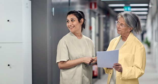 Två personer i gula sjukhuskläder står i en korridor och tittar åt sidan.