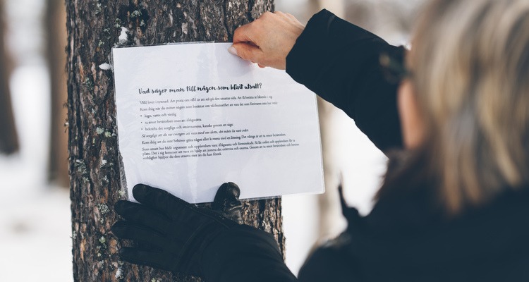 enhetschef Bitte Westerlund sätter upp en lapp på ett träd, med frågor om våld i nära relation, för frågeslingan de har på arbetsplatsträffar om det. 