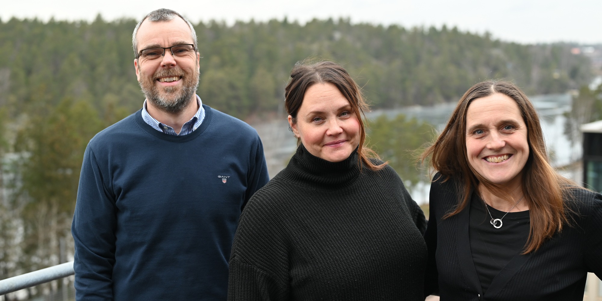 Tre personer står på en balkong och tittar mot kameran.