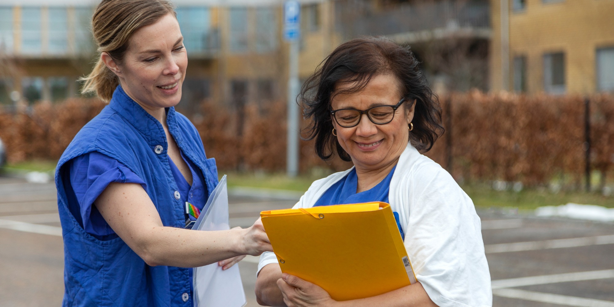 Två leende sjuksköterskor tittar på en journal tillsammmans