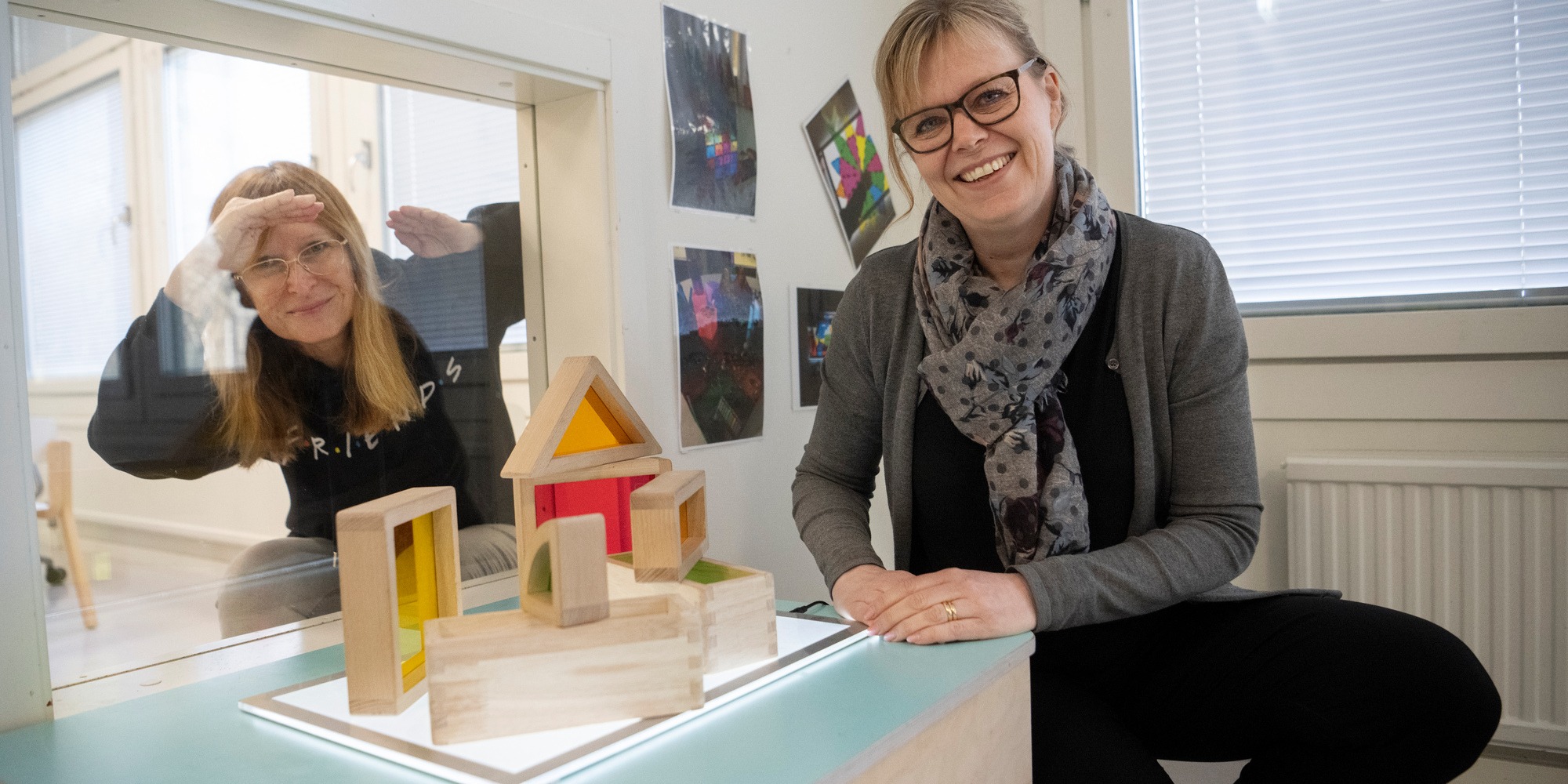 Kollegorna Annica Lindell (i förgrunden) och Tina Karlson (bakom glasrutan) vid ett ljusbord med klossar med färgat glas som barnen kan undersöka. Plats Förskolan Vitsippan i Sundbyberg.