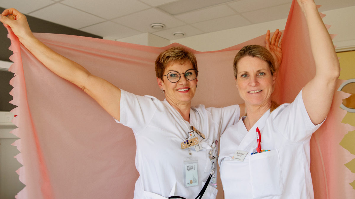 Dusanka Kravljanac och Malin Lindell håller upp en rosa spilerdug i ett patientrum.