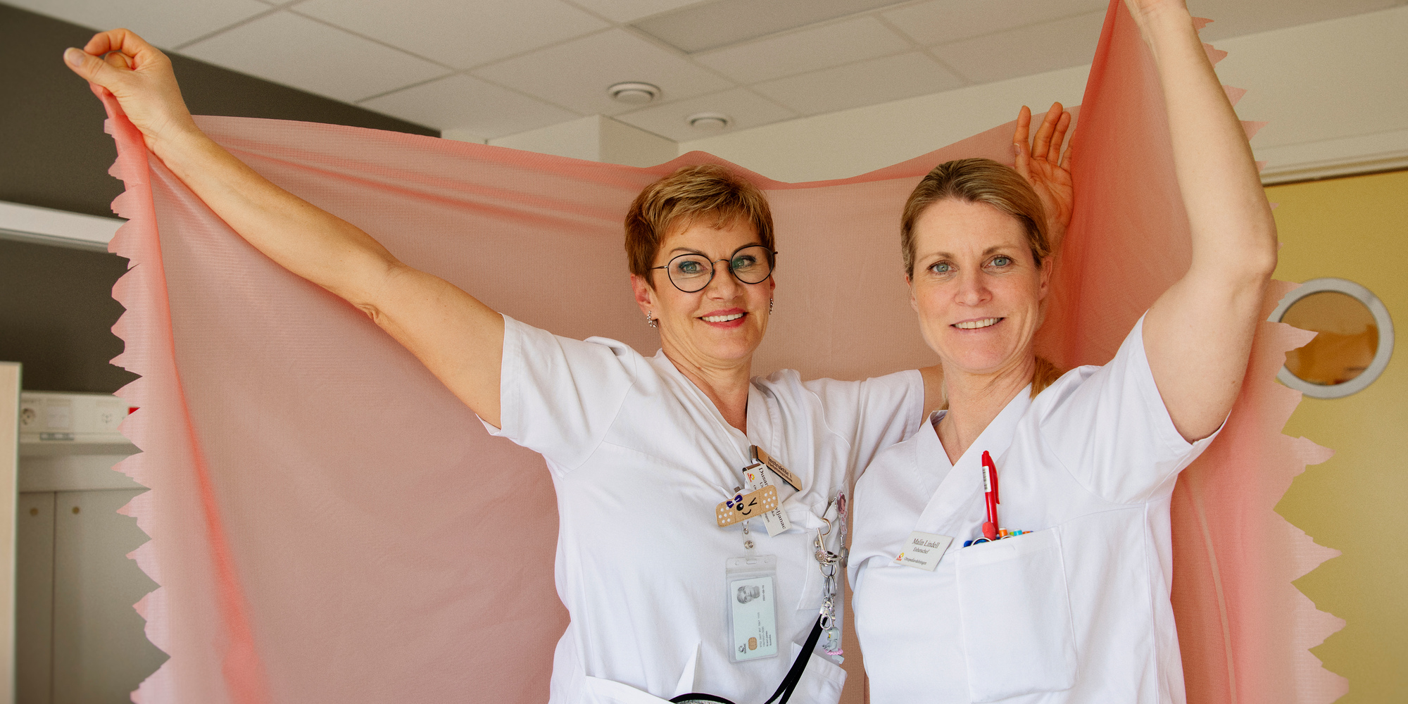 Dusanka Kravljanac och Malin Lindell håller upp en rosa spilerdug i ett patientrum.