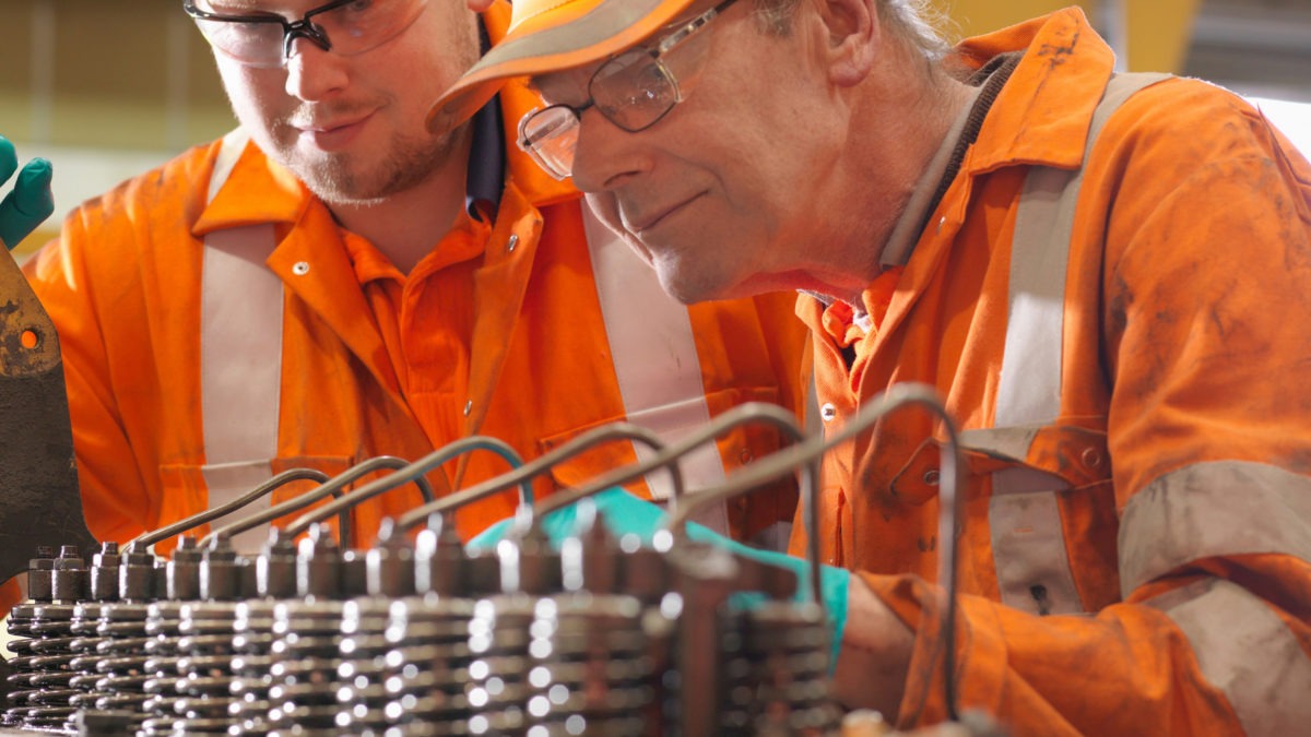 två män i orange arbetskläder studerar en generator