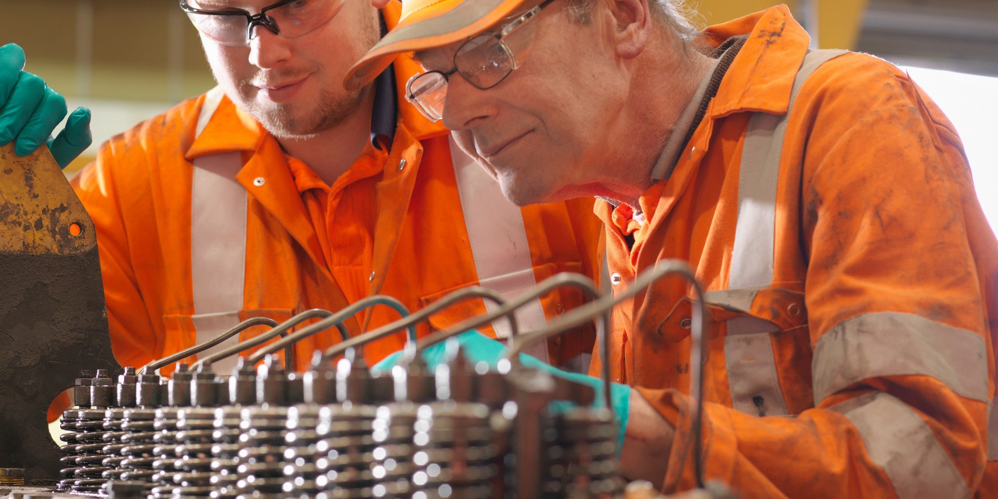 två män i orange arbetskläder studerar en generator