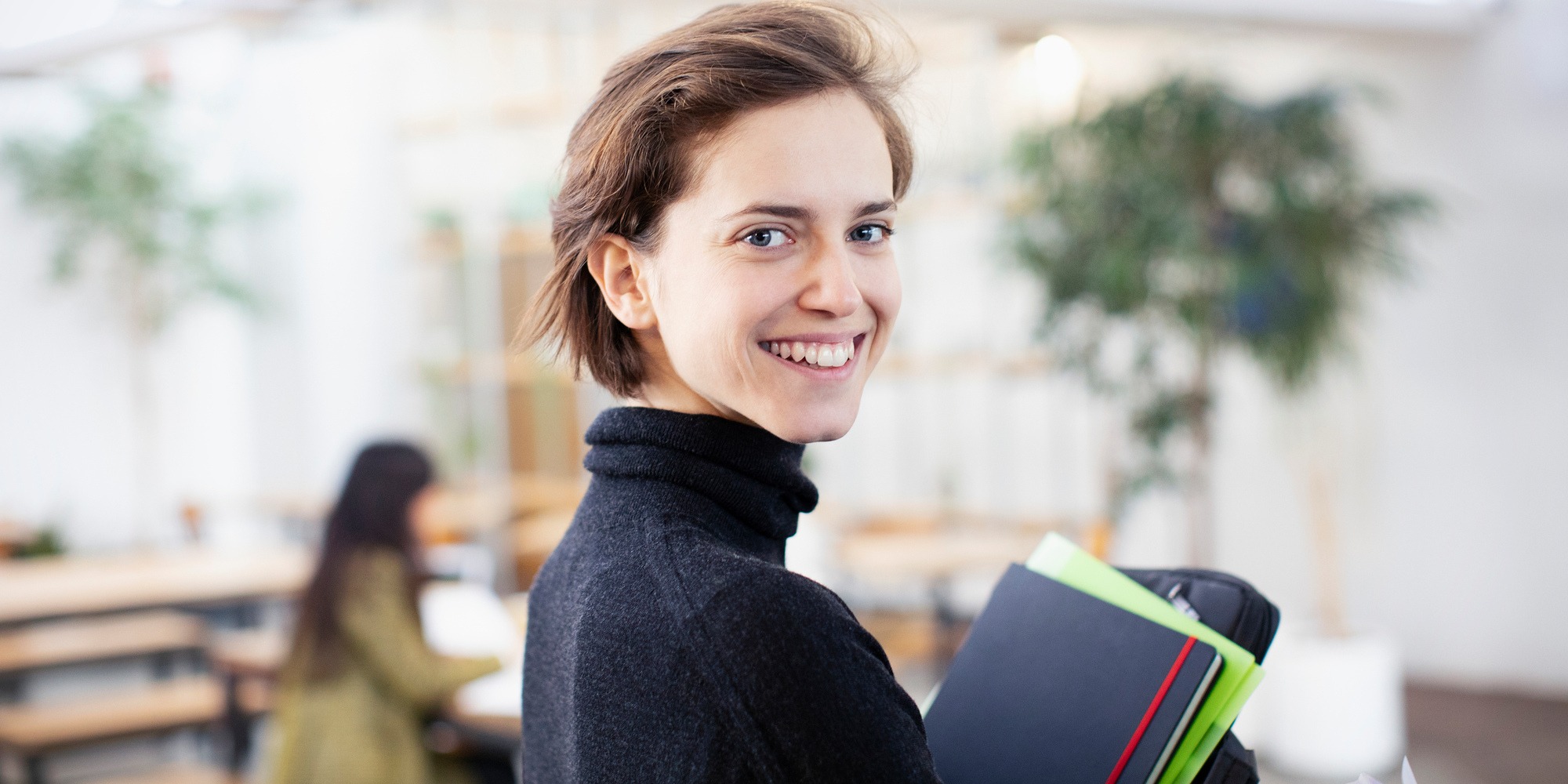 ung kvinna ler med pärmar i famnen på jobbet