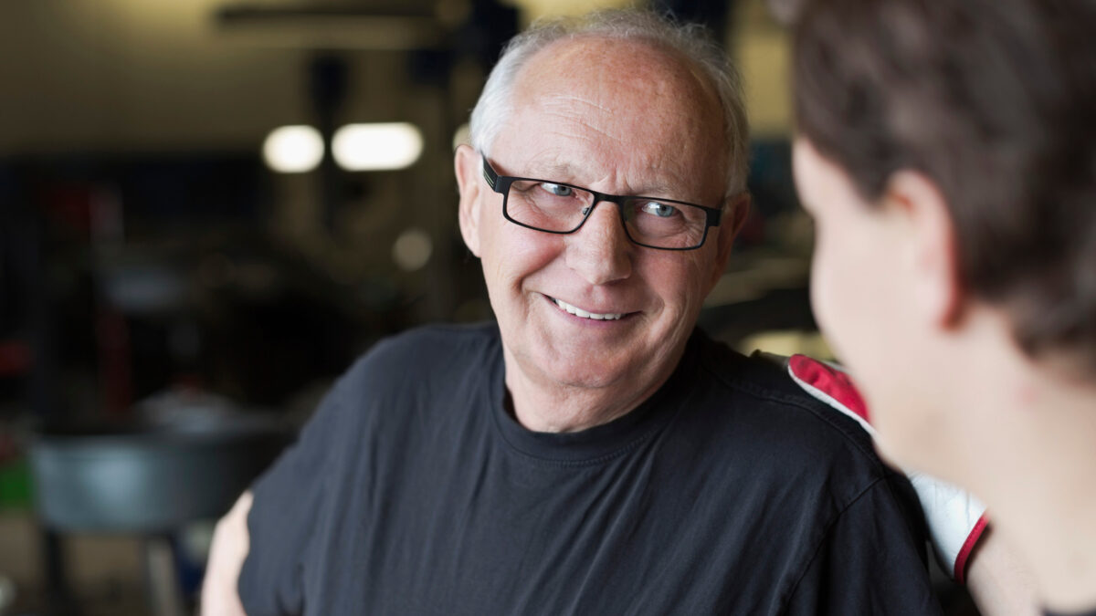 Glad äldre bilmekaniker pratar med ung bilmekaniker i bilverkstad