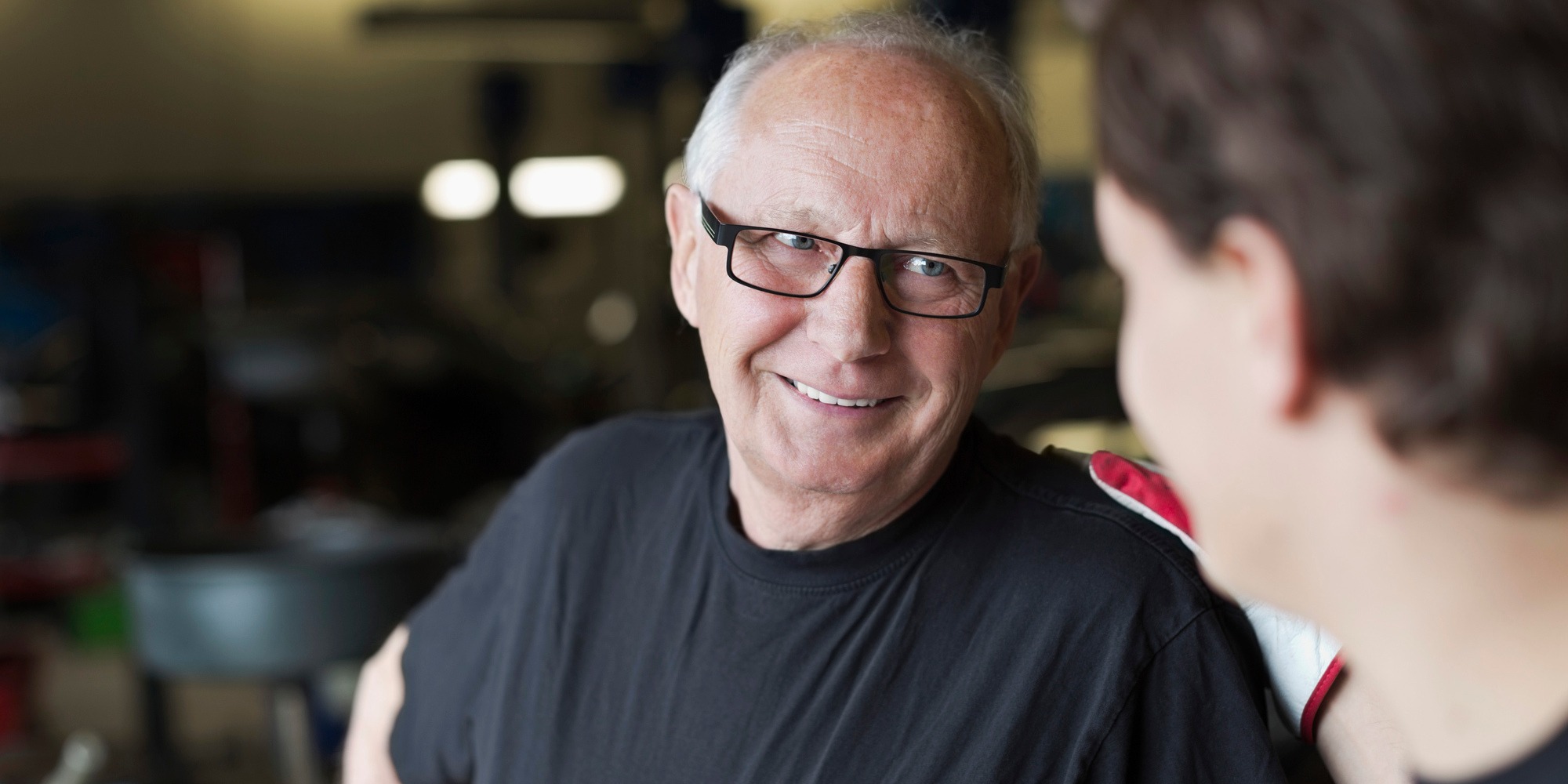 Glad äldre bilmekaniker pratar med ung bilmekaniker i bilverkstad