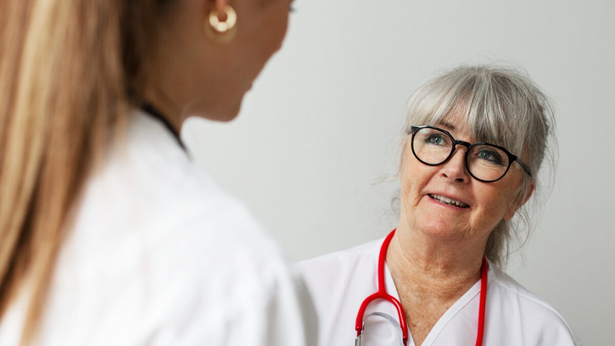 två kvinnor i vårdarbetskläder talar med varandra