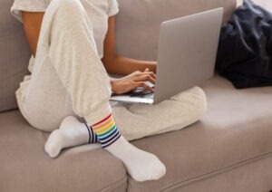 Kvinna i mysdress med laptop i soffa, distansarbete.