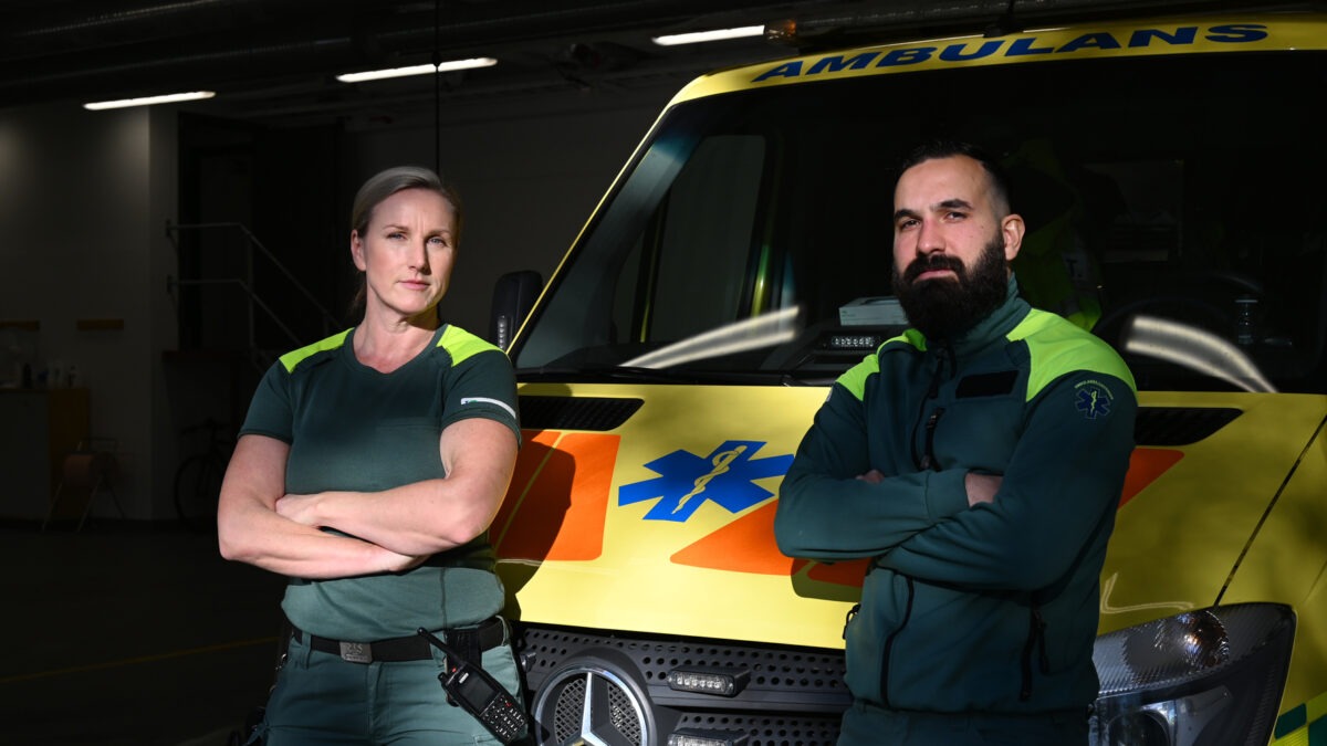 Två ambulanssjukvårdare står framför en ambulans med armarna i kors