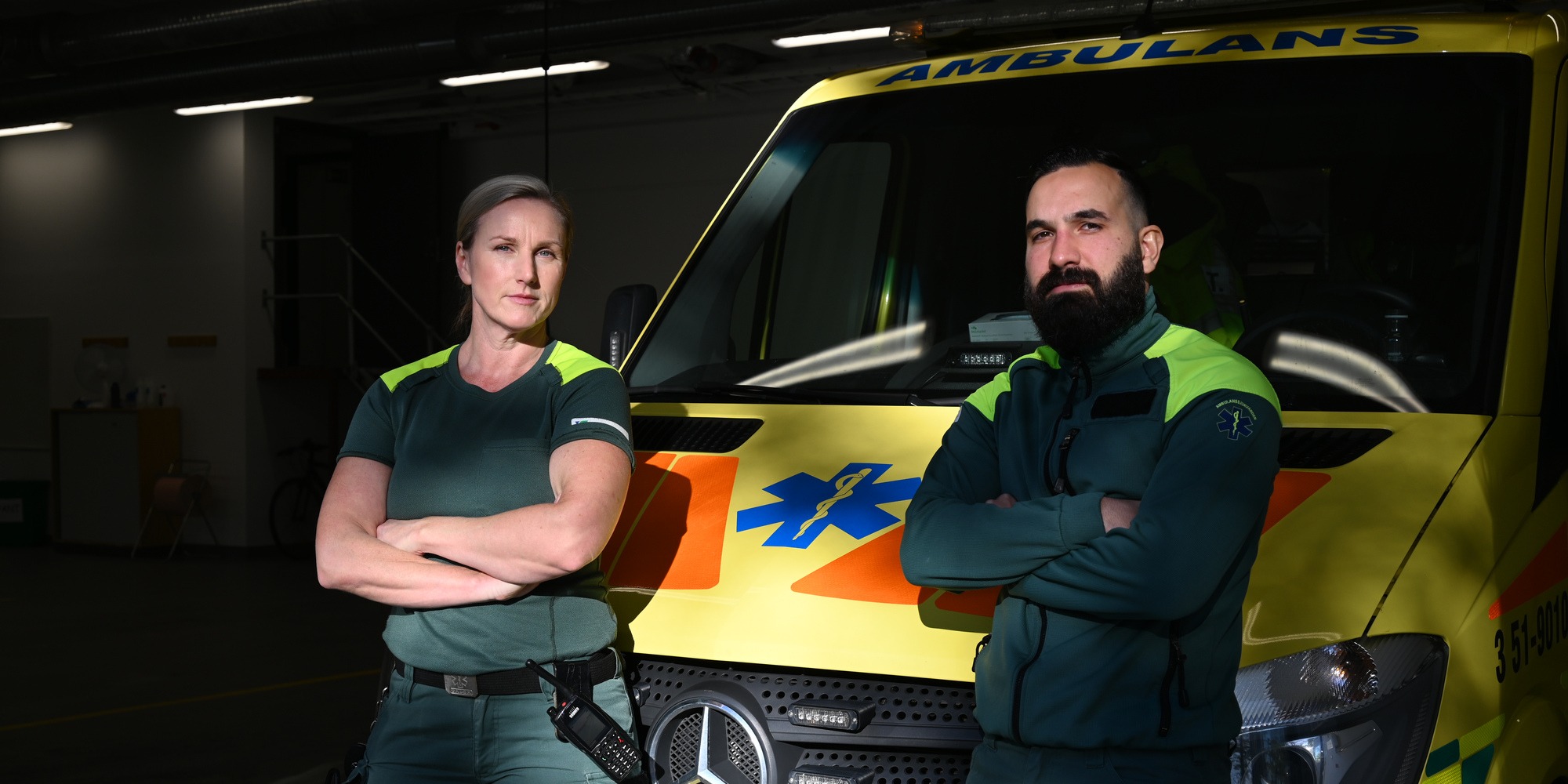Två ambulanssjukvårdare står framför en ambulans med armarna i kors