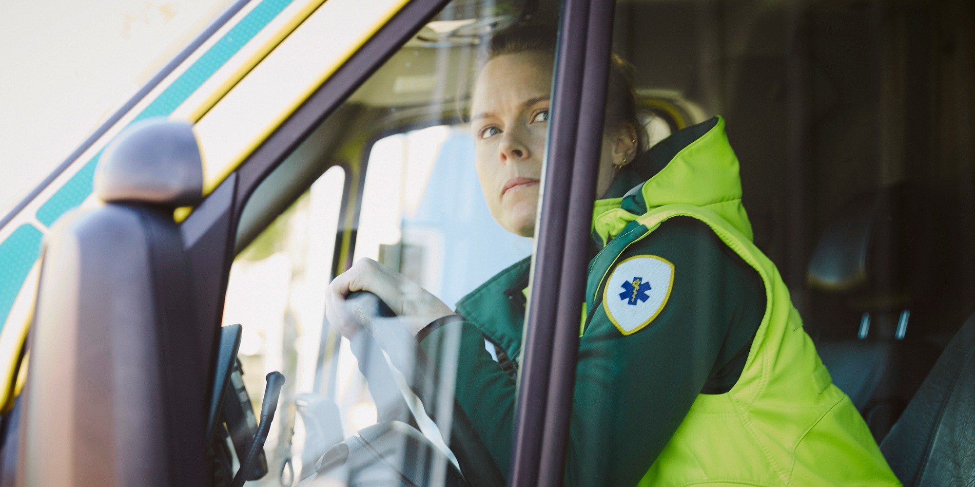 Ambulanspersonal kvinna i ambulans förarsäte, tema hot och våld på arbetsplatsen.