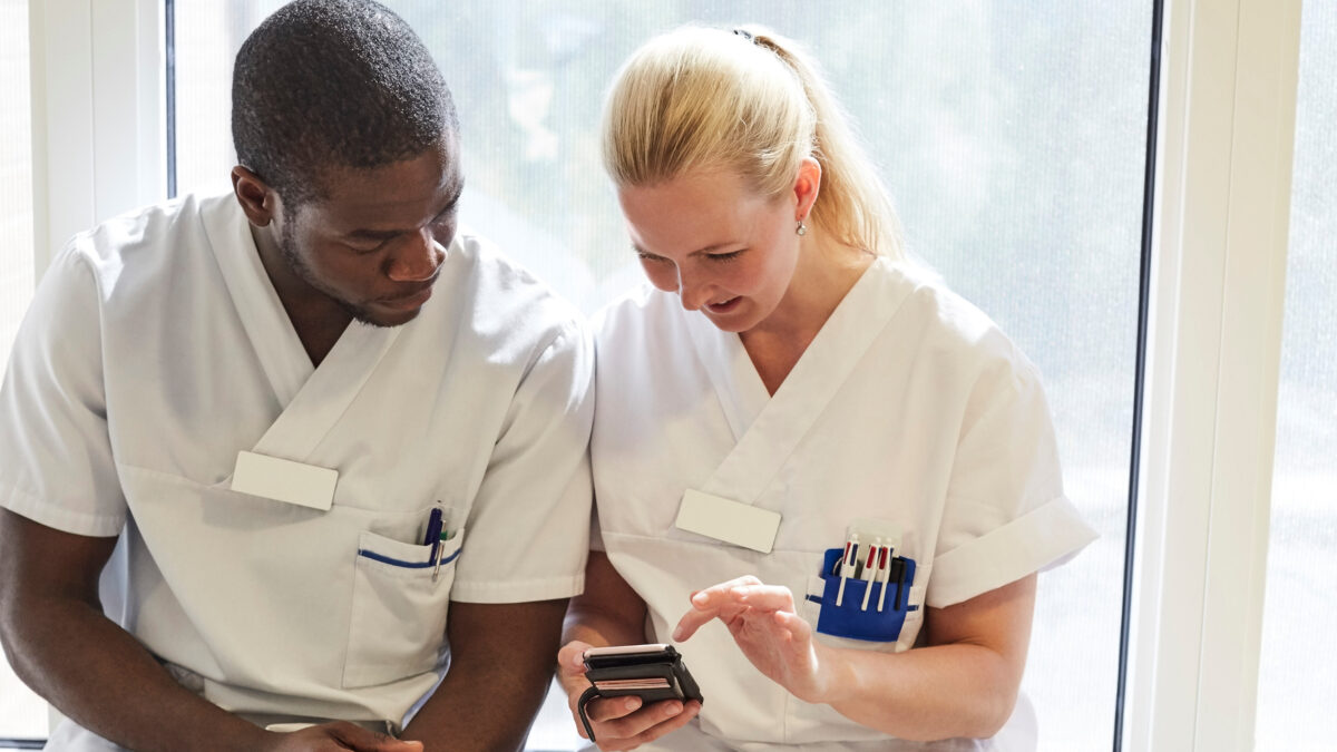 Sjuksköterskor använder mobiltelefoner vid fönster på äldreboende