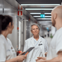 tre personer i vårdarbetskläder samtalar med varandra i en sjukhuskorridor