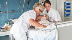 två undersköterskor vänder en patient i en sjukhussäng