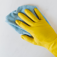 Hand med gul gummihandske håller en blå trasa.
