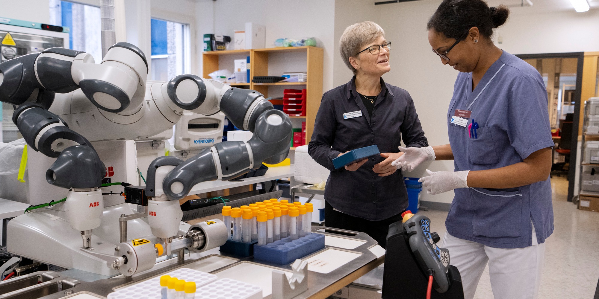 En robot med två armar flyttar provrör. I bild också två personer: lena Nyman, chef, och Shukri Omar, Biomedicinsk analytike, på Preanalytiska sektionen, karolinska sjukhuset.