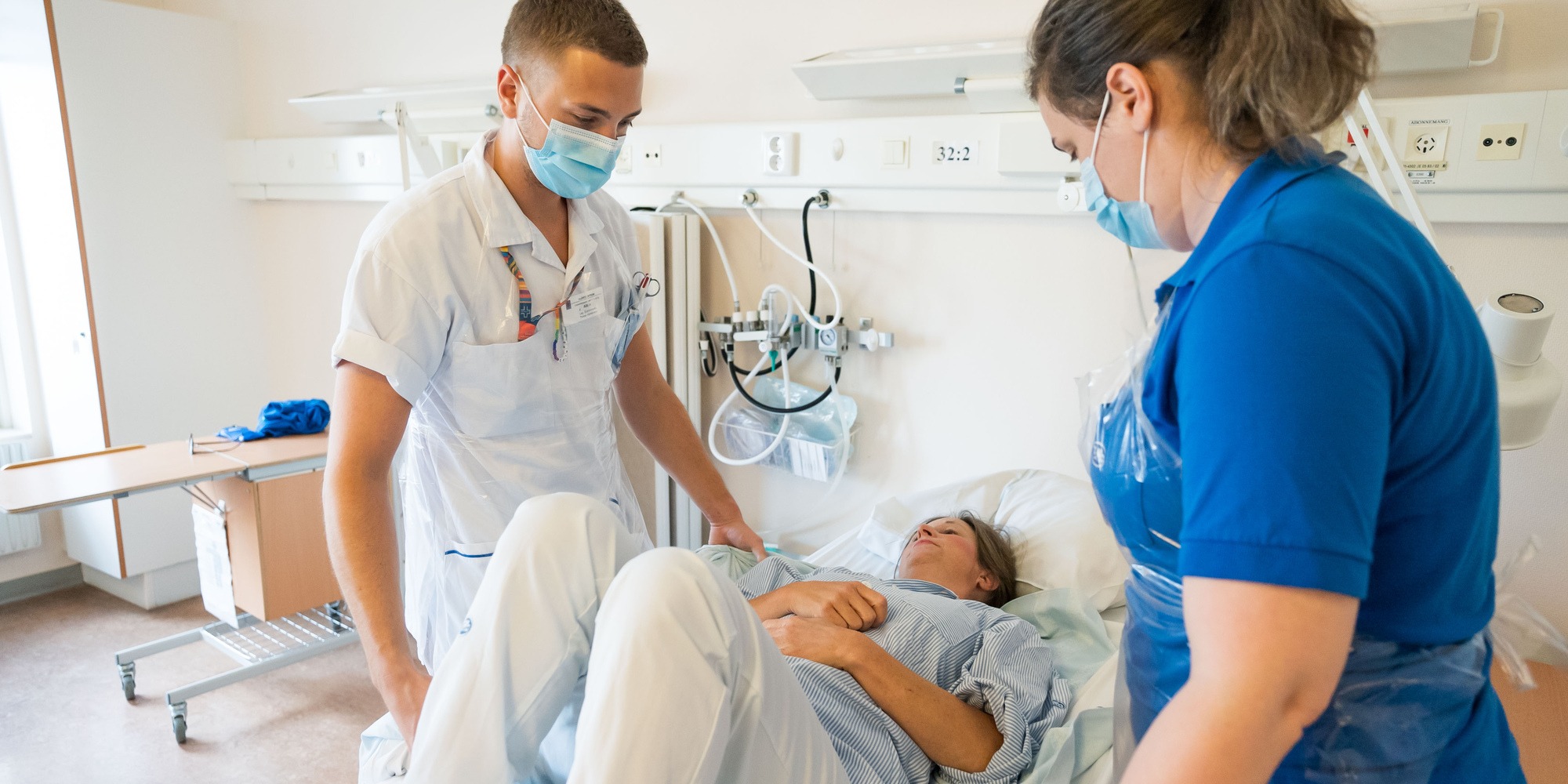 Vårdpersonal hjälper patient i säng, tema säkra personförflyttningar.