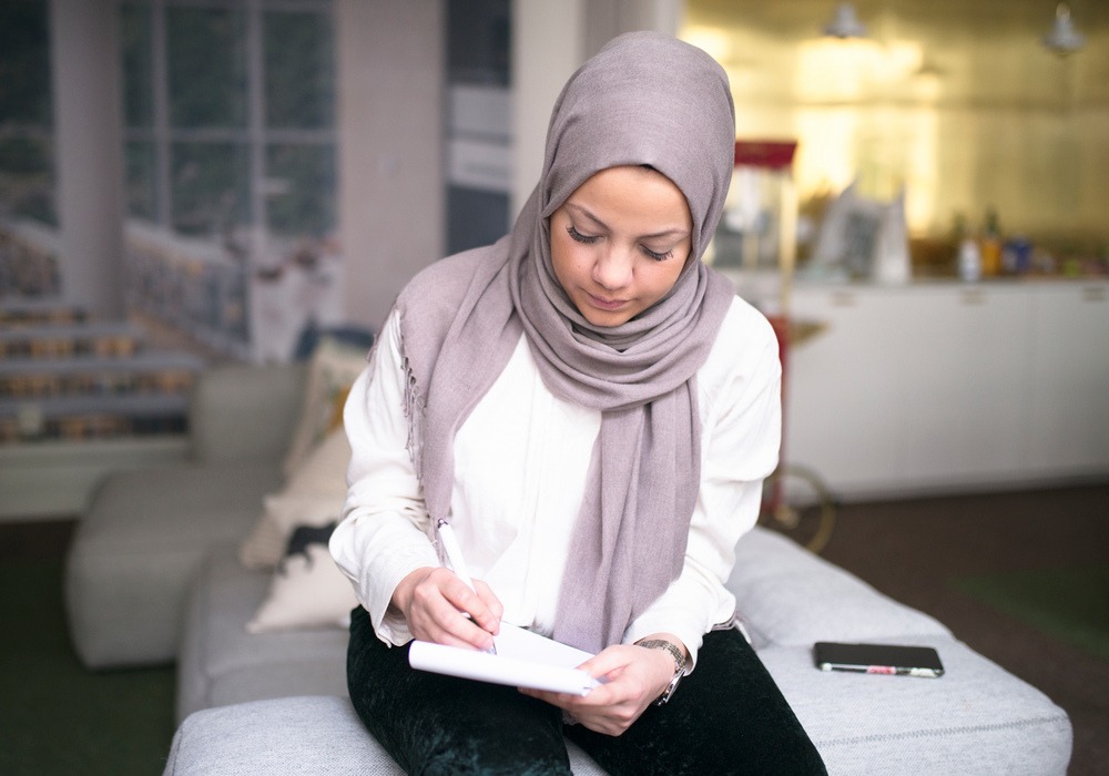 kvinna sitter på soffa i kontorsmiljö och antecknar.