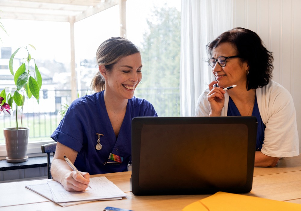 Två leende sjuksköterskor jobbar ihop framför datorn