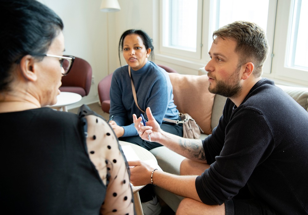 tre personer talar med varandra, sittandes i en soffgrupp.