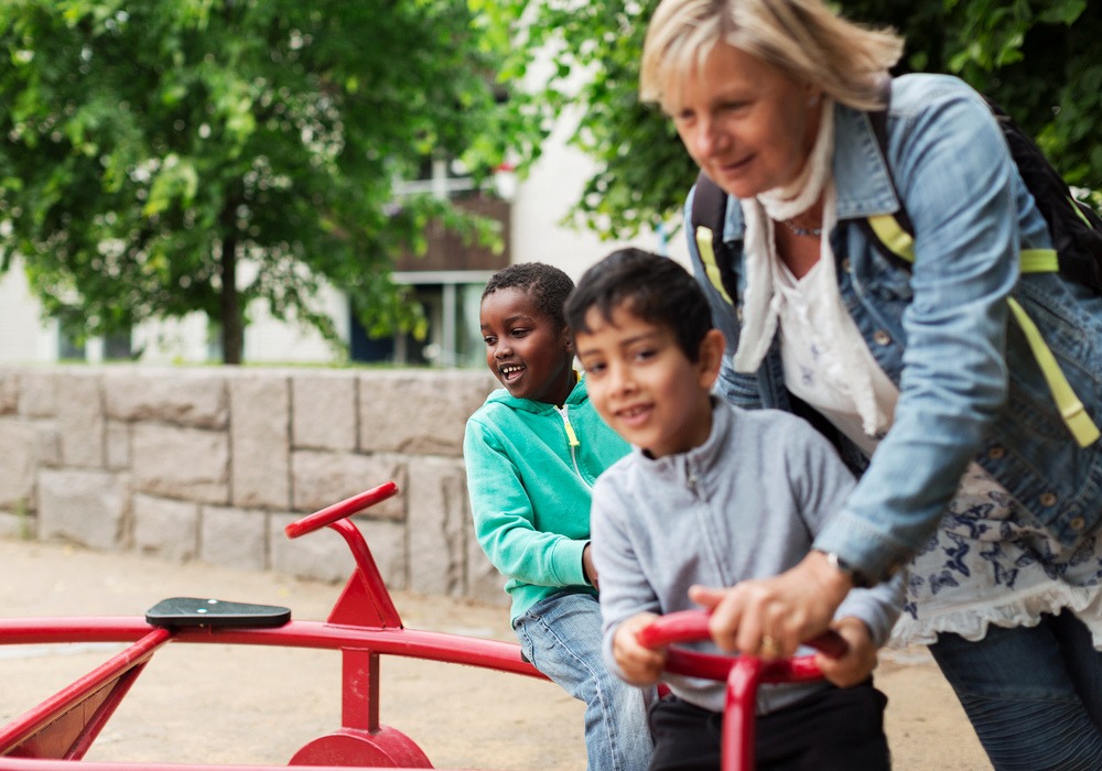 vuxen kvinna hjälper två små pojkar att åka cykelkarusell i en lekpark