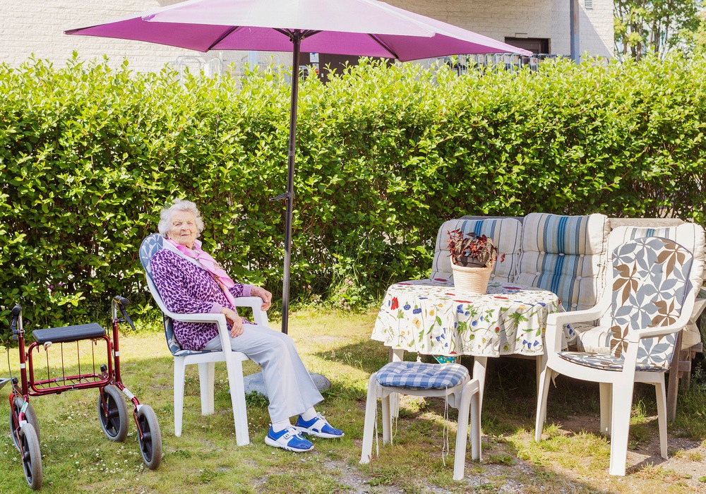 Äldre kvinna sitter utomhus i skuggan.