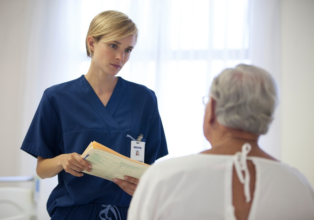 En person i sjukvårdskläder talar med en man i sjukhuskläder.