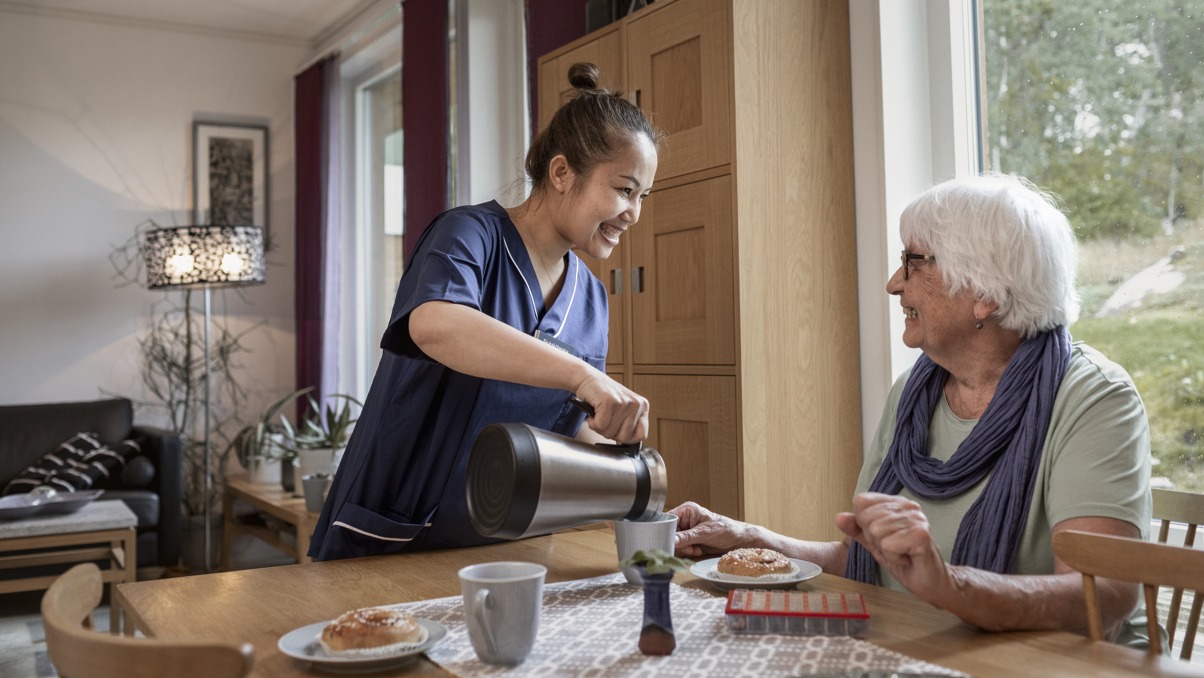 Kvinna som jobbar i hemtj&auml;nsten h&auml;ller upp kaffe till brukare.