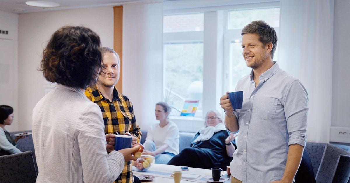 Tre personer står upp och fikar