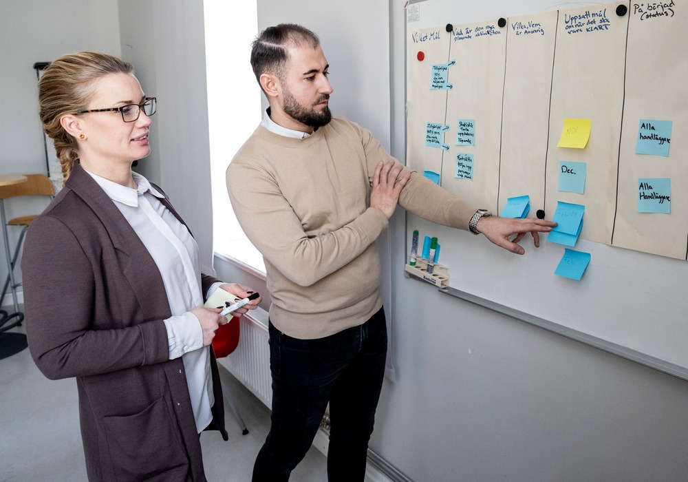 Kvinna och man står vid whiteboard med lappar, tema bemanning.