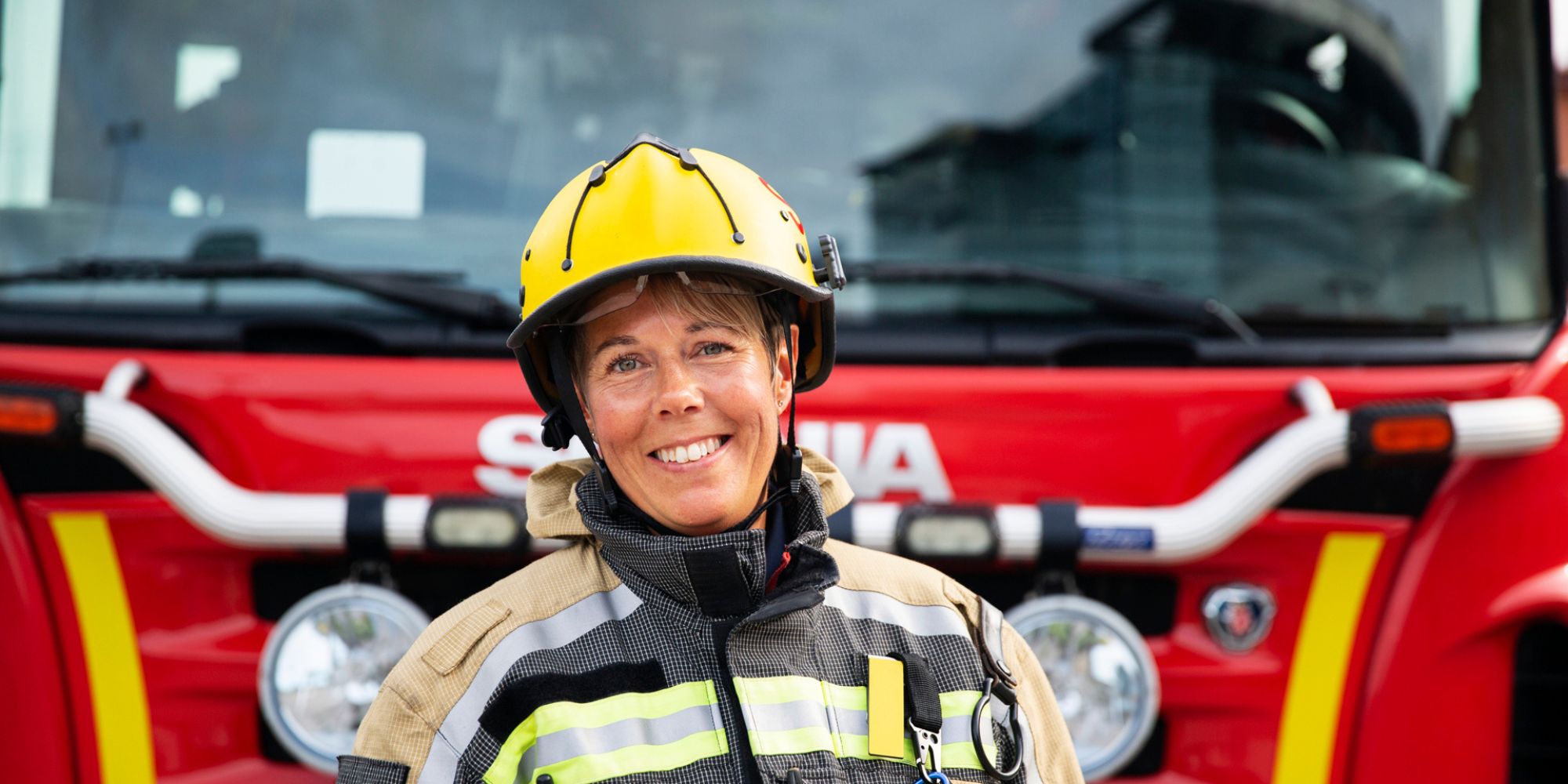 Kvinnlig brandman som ler och står framför en brandbil.