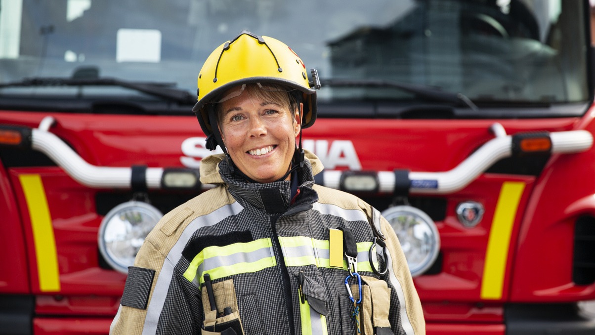 Kvinnlig brandman som ler och står framför en brandbil.