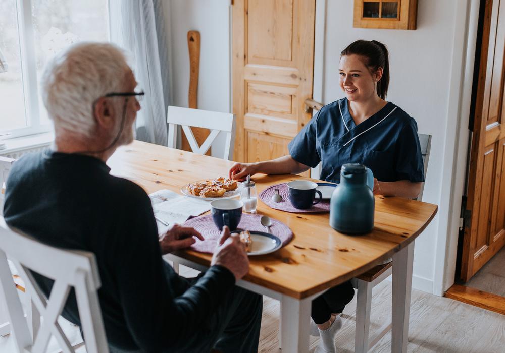 Kvinnlig hemtjänstpersonal fika hemma hos äldre man