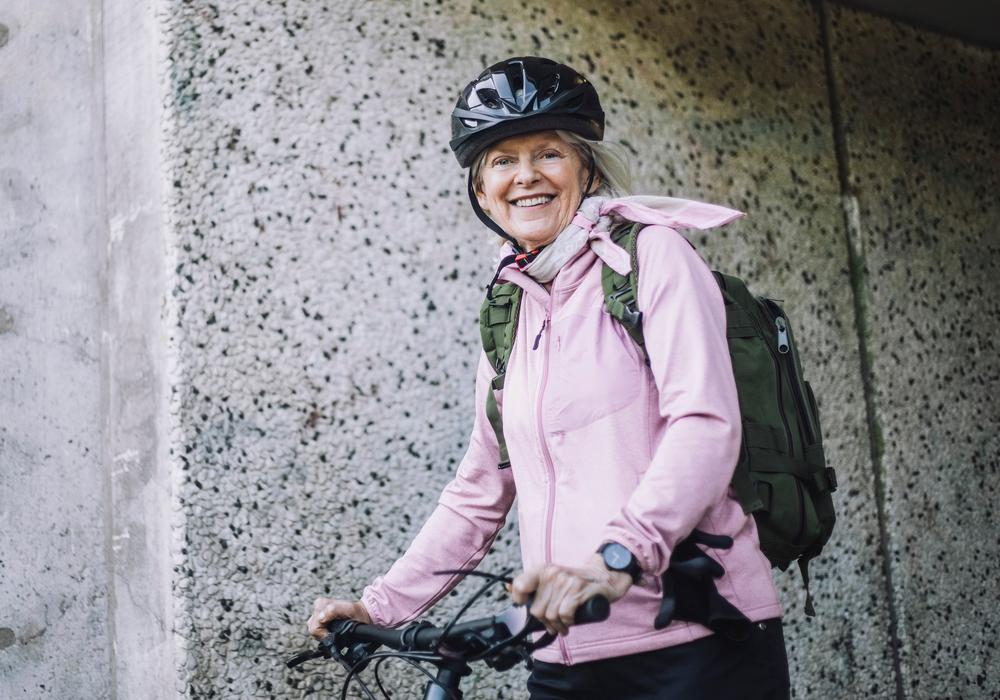 En leende kvinna med cykel och cykelhjälm tittar mot kameran.