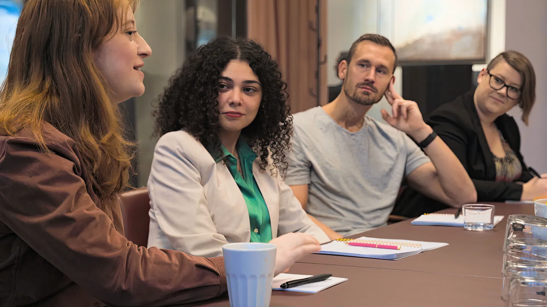 Fyra kollegor i möte vid ett konferensbord. En kvinna pratar och tre kollegor lyssnar och anteckningar.