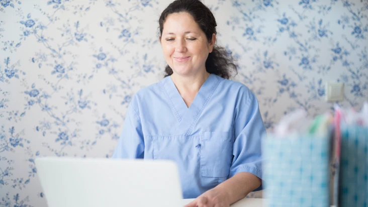 Digifysisk arbetsmiljö. En kvinna i sjukvårdskläder framför en laptop