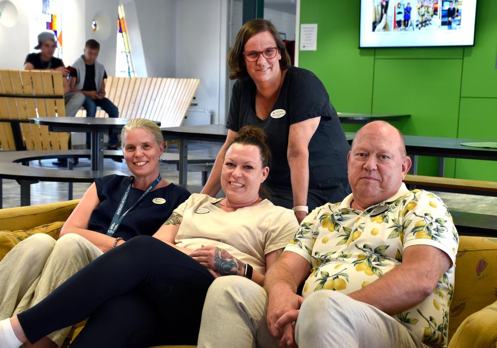 Skolpersonal sitter och står vid soffa i uppehållsrum. Två är rektorer, två är lärare och arbetsmiljöombud.