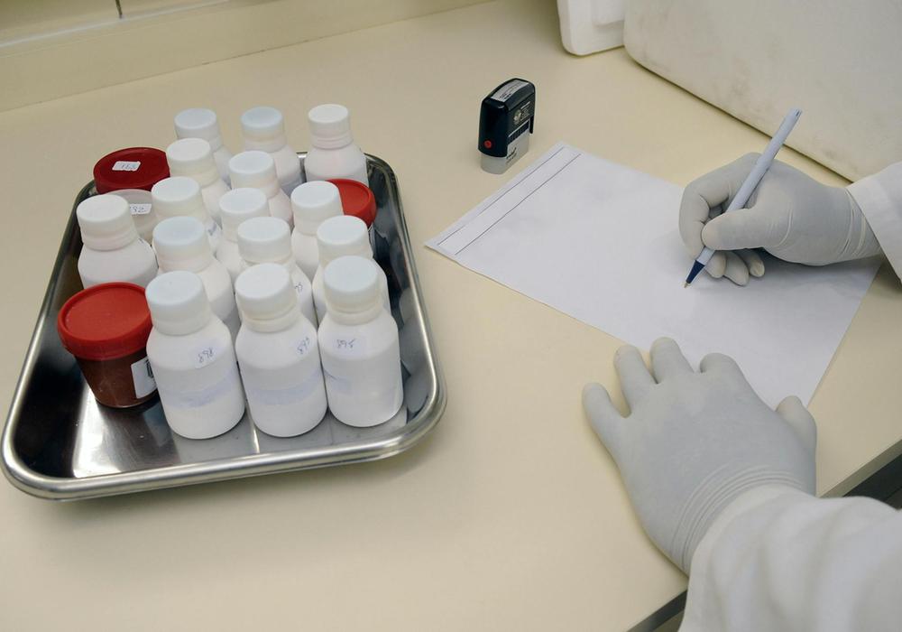 Närbild händer med handskar som antecknar, bredvid står en bricka med medicinburkar.