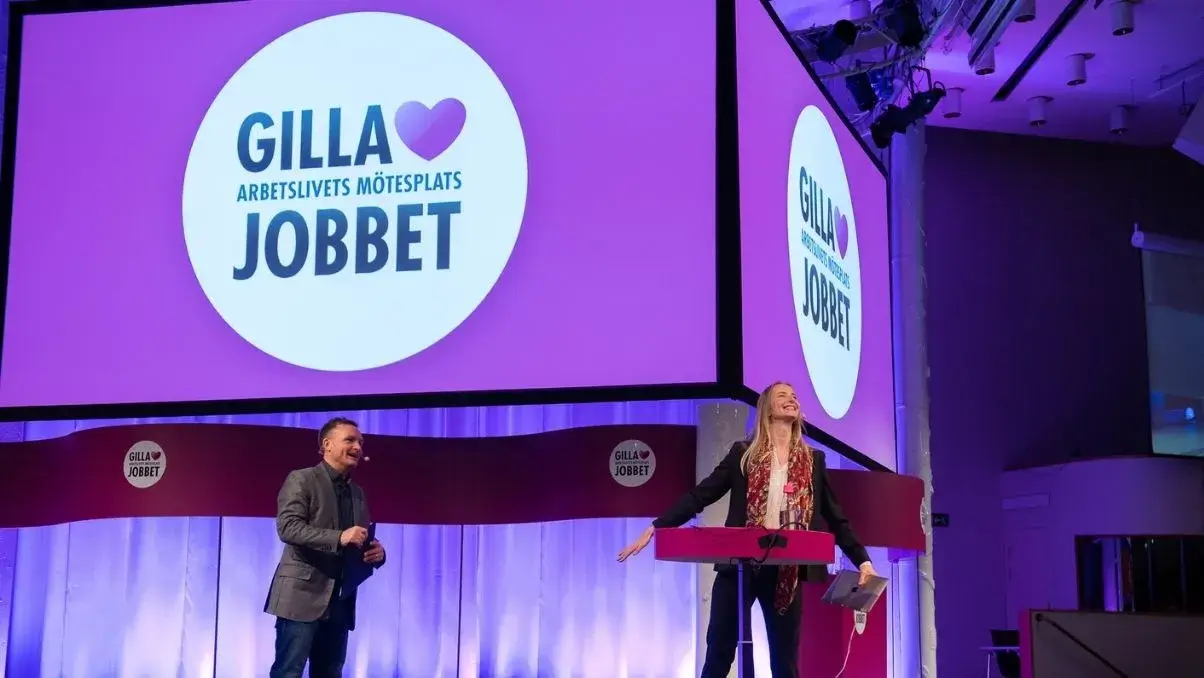 Två personer på scen med bakgrund Gilla jobbet