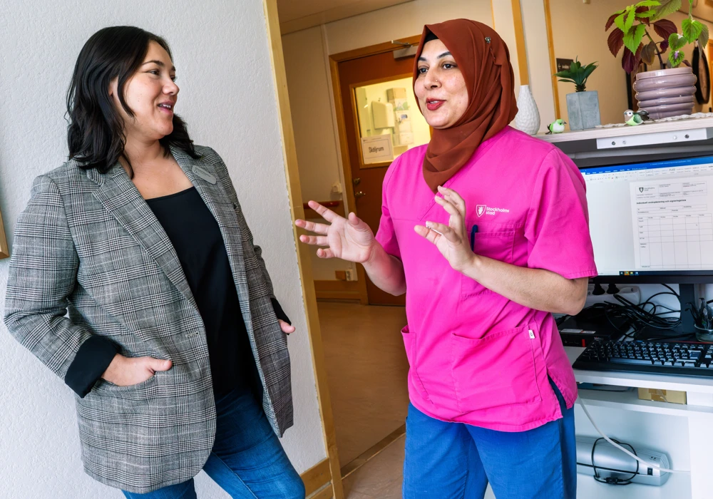 Katarina Näreskog, enhetschef och Rahana Akter, undersköterska, samtalar i en korridor med en dator i bakgrunden.