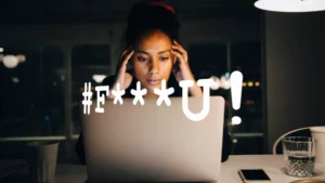 Ung kvinna sitter framför en laptop och ser allvarlig ut. Ett ord är skrivet i bilden som signalerar att hon har fått ett hot/hatmejl.