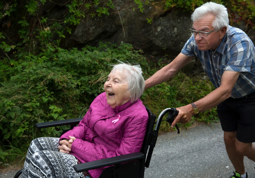 Vad är viktigt för dig? En man drar en glad kvinna i rullstol på en skogsväg.