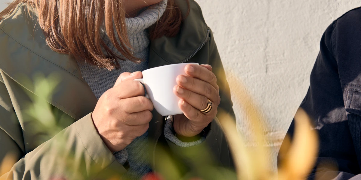 En kvinna som håller i en kopp kaffe medan hon sitter på en bänk.
